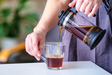 Glass press teapot in the hand of a waitress. Cafe with a cozy home atmosphere and interior.