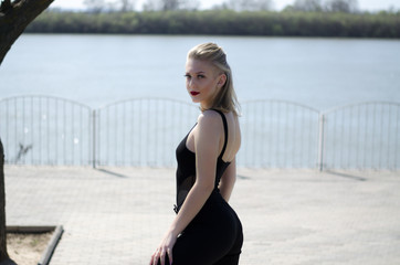 Beautiful young model. The blonde poses in nature. Red lipstick on the lips. Model in black body.