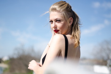 Beautiful young model. The blonde poses in nature. Red lipstick on the lips. Model in black body.