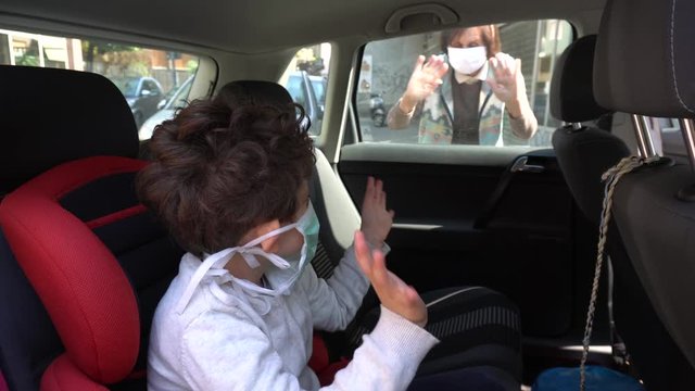 Europe, Italy , Milan - life stile during n-cov19 Coronavirus outbreak epidemic - children boy five years old in the car with mask speaks and say hello to grandmother 1 meter distance security 