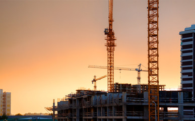 Fototapeta na wymiar View of the building process. Construction site with cranes and monolithic buildings against the sunset sky