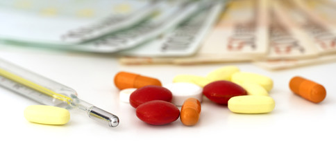 Pills, tablets and medical thermometer, blurred euro bills on the background. Selective, soft focus.