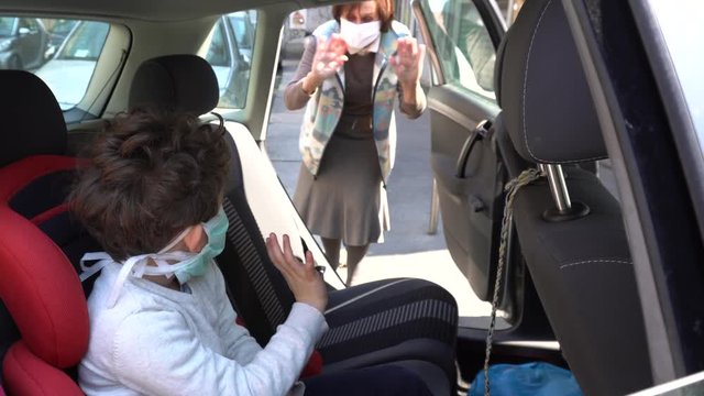 Europe, Italy , Milan - life stile during n-cov19 Coronavirus outbreak epidemic - children boy five years old in the car with mask speaks and say hello to grandmother 1 meter distance security 