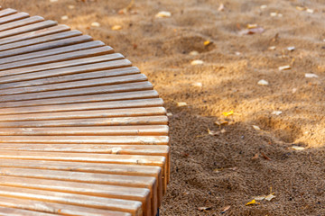 Abstract background texture. Fragment of a wooden semicircular bench on a background of sand with autumn leaves