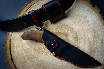 hunting knife with a fixed handle in a sheath made of genuine black leather stitched with red thread, handmade on a wooden saw cut of a tree, top view