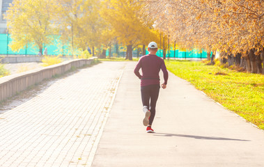 Athlete runner runs away into the autumn park on a sunny day