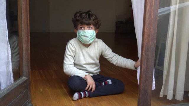 Europe, Italy , Milan - life stile during n-cov19 Coronavirus outbreak epidemic - children boy five years old  with mask during a boring day,  say hello outside the window - quarantine at home 