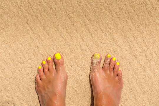 Female feet in the sand on a beach with yellow nail polish