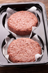 two pieces of ground meat substitutes for vegetarian burgers in plastic box on wooden background