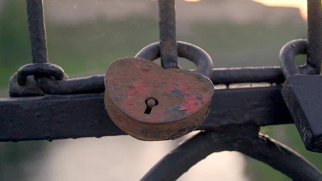 rusty heart-shaped lock fastened on a fence of metal bars