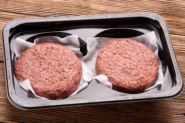 two pieces of ground meat substitutes for vegetarian burgers in plastic box on wooden background