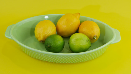 trois citrons et deux limes dans un plateau sur un arrière plan de couleur jaune