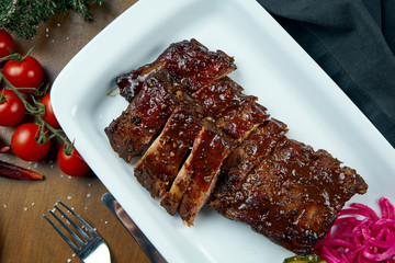 Close up view on tasty delicious bbq coocked ribs with barbecue sauce in white plate on wooden background. Classical american Barbecued Pork in composition with ingridients