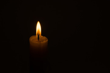 Glowing candle in the dark. Burning wick candles on a black background with copy space. The concept of sorrow