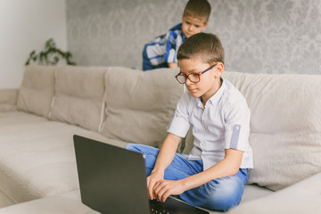 A schoolboy in glasses holding a video conference with a tutor on a laptop at home, sitting on the couch. The concept of distance learning.