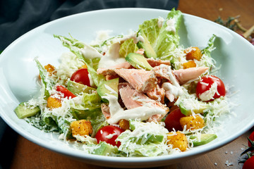 Close up view on served Caesar salad with smoked Salmon in white plate on wooden background. Tasty seafood salad