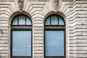 A sculpture of Medusa's head with snakes and a sculpture of a mature bearded man's head adorn the keystones above a pair of window arches on an old building in Budapest, Hungary.