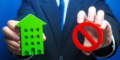 Man holds a green house and red prohibition symbol NO. Prohibition of operation. Denial of...