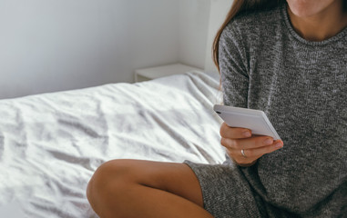 yong woman  wearing gray casual dress using smartphone and siiting on the bed ,close up phone in female hands copy space