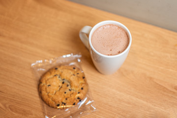 A mug of cocoa on a wooden table next to an oatmeal cookie. The view from the top.