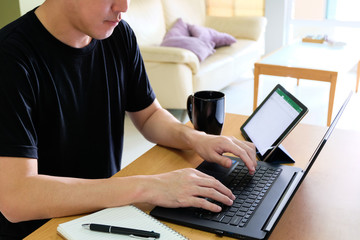 Selective focus of men sitting in living room wear casual dress working from home by typing computer keyboard and also vedio conference meeting with co-worker with tablet and mobile phone. Home office