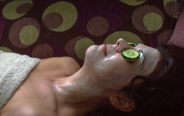 Natural beauty treatment at home: Woman using organic anti aging mask and cucumber for dark circles.