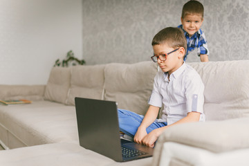 A schoolboy in glasses holding a video conference with a tutor on a laptop at home, sitting on the couch. The concept of distance learning.