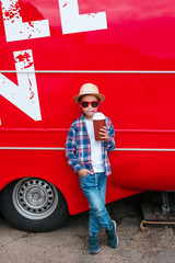 Little boy in sunglasses and hat is drinking milk cocktail over red city background