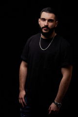 close-up of a dramatic portrait of a young serious guy, musician, singer, rapper with a beard in black clothes on a black isolated background