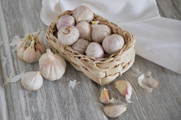 White round garlic lies in a wicker basket on a white light wooden background with salsify