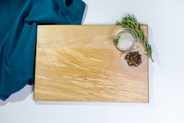 Wooden cutting board with fresh rosemary and seasonings. Top view copy space on light background. Blue towel in the corner