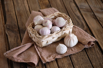 White round garlic lies in a wicker basket on a brown wooden background with a dark napkin. Close-up photo
