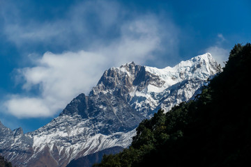 Obraz premium View on Himalayas, Annapurna Circuit Trek, Nepal. Early morning in the mountains. Lower parts of the mountains covered in shadow, high snow caped mountains peaks catching the first beams of sunlight