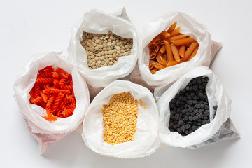 Multi colored legume pasta and beans in paper bags on white background. Red and yellow lentil paste, green lentils, black chichpeas. Vegan diet concept. Vegetable protein. Trend healthy food.Top view.