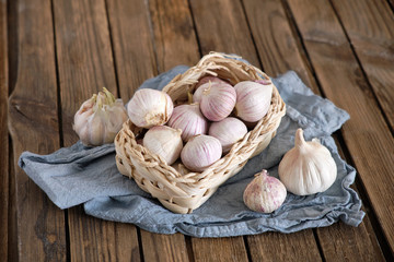 White round garlic lies in a wicker basket on a brown wooden background with a blue napkin. Close-up photo