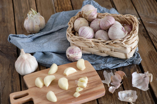 White round garlic lies in a wicker basket on a brown wooden background with a blue napkin. Next to the cut garlic clove and a knife. Close-up photo