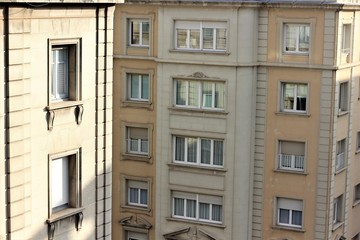 Fototapeta na wymiar sunny windows on the upper floors of two beige buildings, one in the foreground, the second in the background.