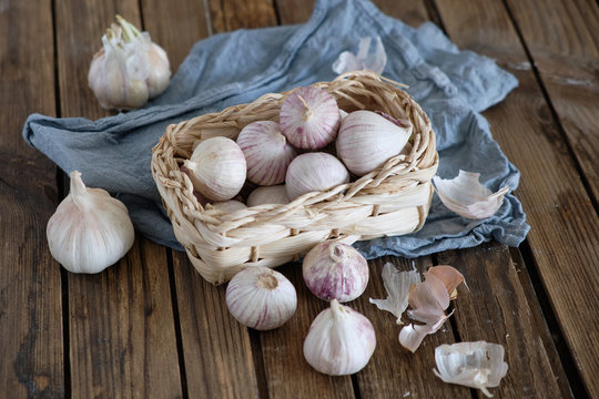 White round garlic lies in a wicker basket on a brown wooden background with a blue napkin. Close-up photo