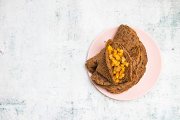 Chocolate brown crepes or thin pancakes with cacao ingredient. Vegan dessert. Copy space. Stuffed with cooked sweet apples