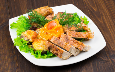 mix of chicken meat with leaves of greens, dill, cheese and a slice of orange in a square white plate on a wooden table