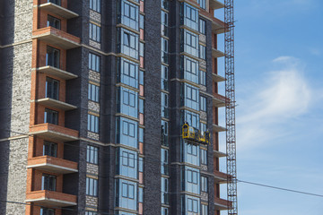 Facade work with construction cradle. Wall decoration of a building under construction with construction cradle