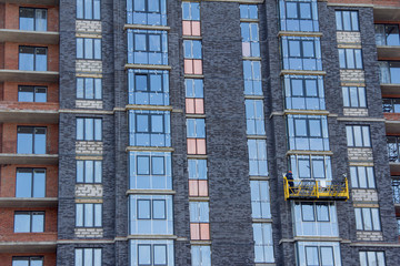 Fototapeta premium Facade work with construction cradle. Wall decoration of a building under construction with construction cradle