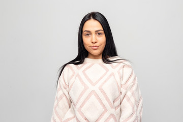 Portrait of a young beautiful cute brunette girl in a warm winter sweater on light gray background.