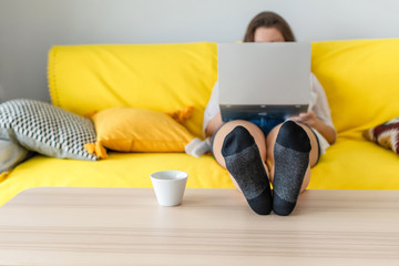 Woman freelancer sitting on the couch with laptops in the socks and putting legs on the table. Work at home. Concept. Cup coffee. Relax at home.