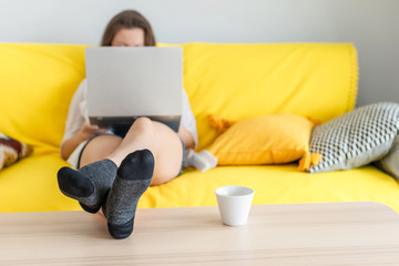 Woman freelancer sitting on the couch with laptops in the socks and putting legs on the table. Work at home. Concept. Cup coffee. Relax at home.