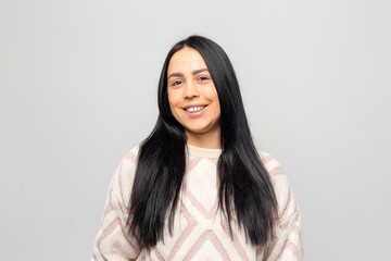 Obraz premium Portrait of a smiling Young beautiful lovely brunette girl in a warm winter sweater on light gray background.
