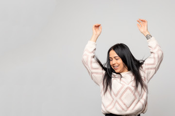 Portrait of a young beautiful cute brunette girl in a warm winter sweater on light gray background.