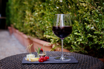 Dessert of various types of cheeses, red currants with a glass of red wine is on the table on the terrace. Dessert for gourmets. Side view, space for text