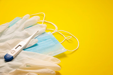 medical latex gloves, protective masks and digital thermometer for protection on yellow background. Useful for pandemic prevention concept