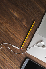 Espacio de trabajo desde casa. Vista cenital de un portátil con auriculares blancos y lápiz amarillo y negro sobre mesa de madera. 